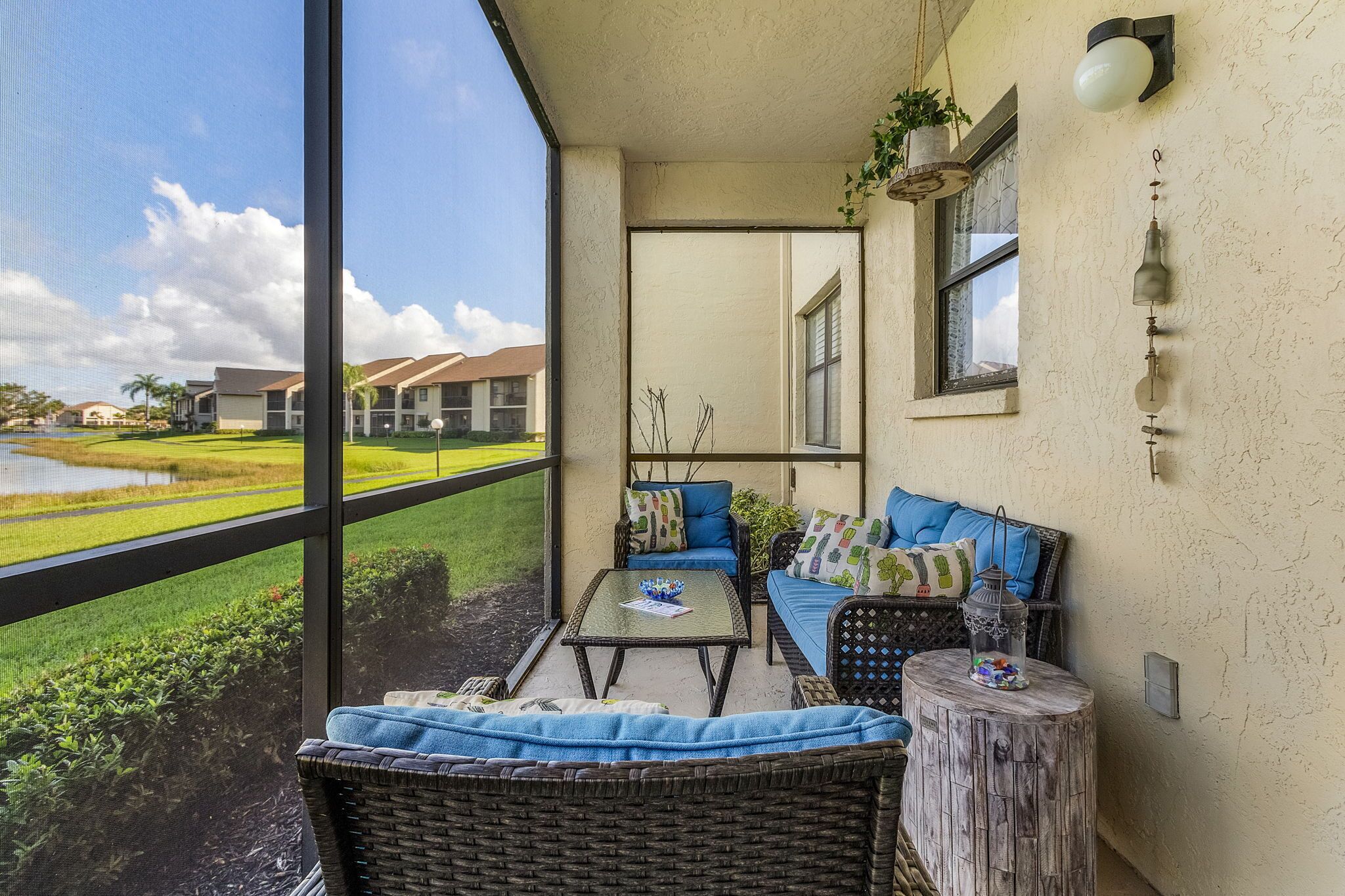 A balcony with wicker furniture, a small table, and a view of a golf course and buildings.