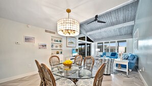Un coin repas avec une table à plateau de verre entourée de chaises en osier, un lustre et une vue sur le salon.