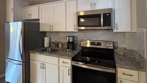 A modern kitchen with white cabinets, stainless steel appliances, and a granite countertop. - Relax in Style: Waikīkī Condo w/ Lanai (Honolulu)