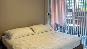 A modern bedroom with a large bed, a ceiling fan, and a view of the outside through a window with blinds. - Relax in Style: Waikīkī Condo w/ Lanai (Honolulu)