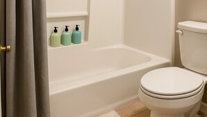 Ein Badezimmer mit einer Badewanne, Toilette und drei Pflegeprodukten auf einem Regal.