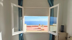 A bedroom with a bed, a window with curtains, and a view of the sea and mountains. - 2222 - MEDITERRANEO A 1-8, HOLIDAYS ON THE ROCKS, 1st LINE OF SEA, PRIVILEGED AREA, SEA VIEW. (Roses)