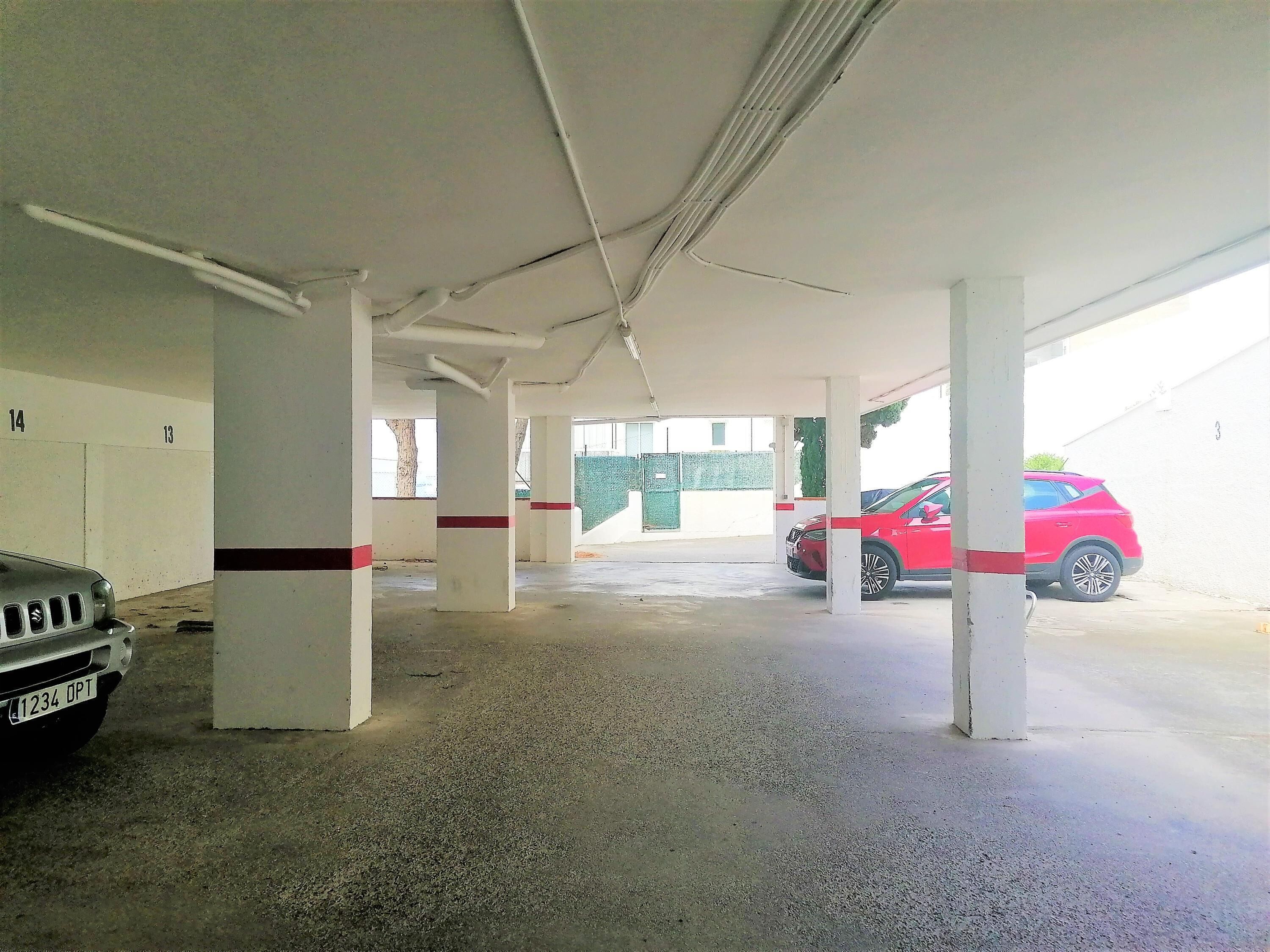 Un parking intérieur avec des piliers en béton et une voiture rouge garée.