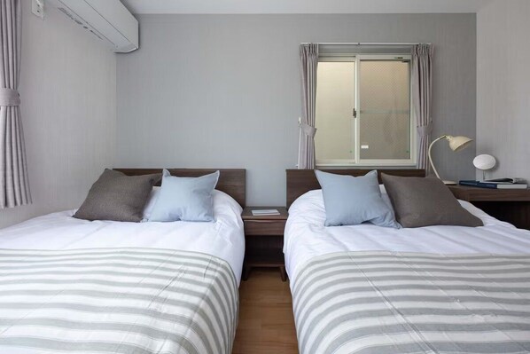 Habitación de hotel con dos camas, una ventana con cortinas, una lámpara de noche y un equipo de aire acondicionado.
