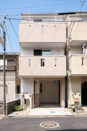 Un edificio residencial de varios pisos con fachada plana, un acceso cubierto y un pequeño jardín con una planta en maceta.