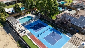 Vue aérienne d’un complexe sportif comprenant un court de tennis, un terrain de basketball et une piscine.