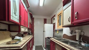 Une cuisine de taille réduite avec des meubles de couleur rouge, un réfrigérateur blanc, une cuisinière et un évier.