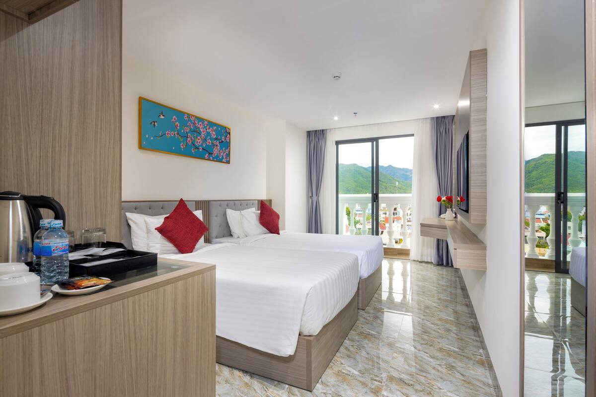 A hotel room with two beds, a balcony with a view, and a breakfast bar with amenities.