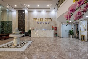Un vestíbulo con mostrador de recepción, suelo de mármol, una fuente y una pared con el texto "PEARL CITY".