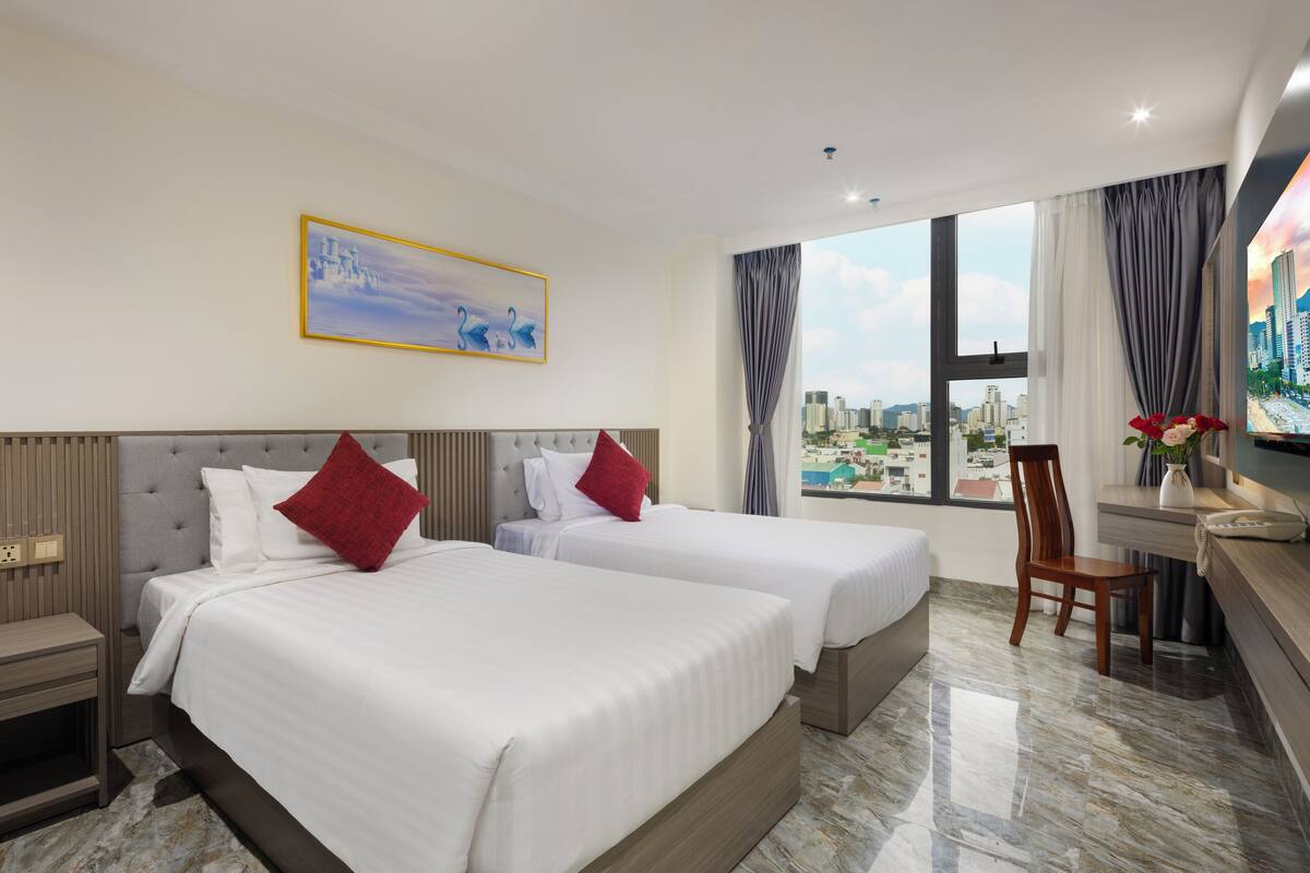 A hotel room with two beds, a desk, and a view of the city.