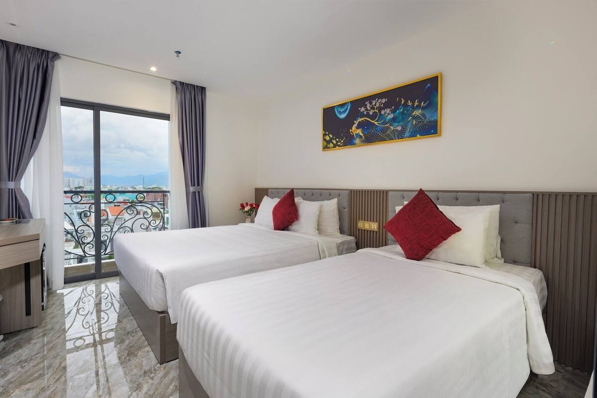 A hotel room with two beds, a balcony with a view, and a painting on the wall.