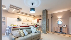 A modern living room with a sofa, a dining area with a kitchen in the background, and a wooden cabinet with a mirror. - [2min InalpiArena] Cozy Suite + A/C + WI-FI (Torino)