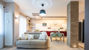 A modern living room with a beige sofa, a dining area with a red kitchen in the background, and a stone pillar. - [2min InalpiArena] Cozy Suite + A/C + WI-FI (Torino)