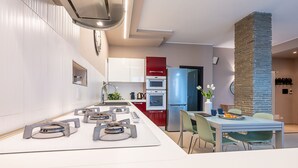 A modern kitchen with white cabinets, a built-in oven, a refrigerator, and a dining area with a table and chairs. - [2min InalpiArena] Cozy Suite + A/C + WI-FI (Torino)
