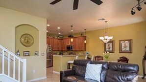 A living room with a leather sofa, a glass coffee table, and a kitchen in the background. - Paseo Grande 3 Bedroom Resort Oasis (Fort Myers)