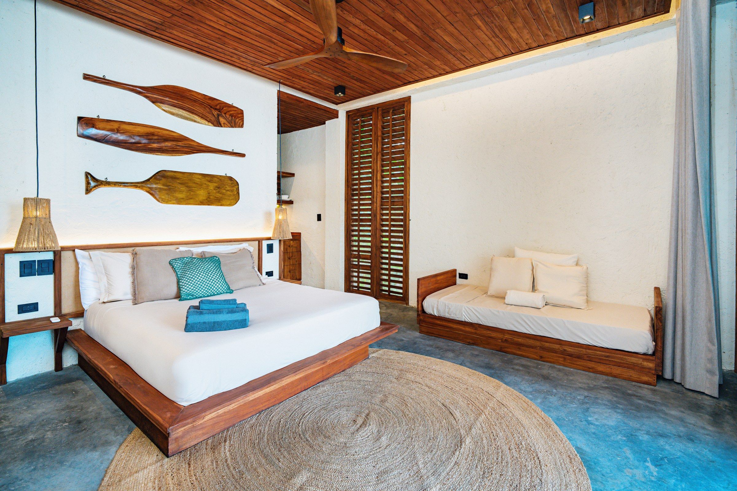 A bedroom with a wooden bed, a smaller sofa, a wall-mounted lamp, and a woven rug.