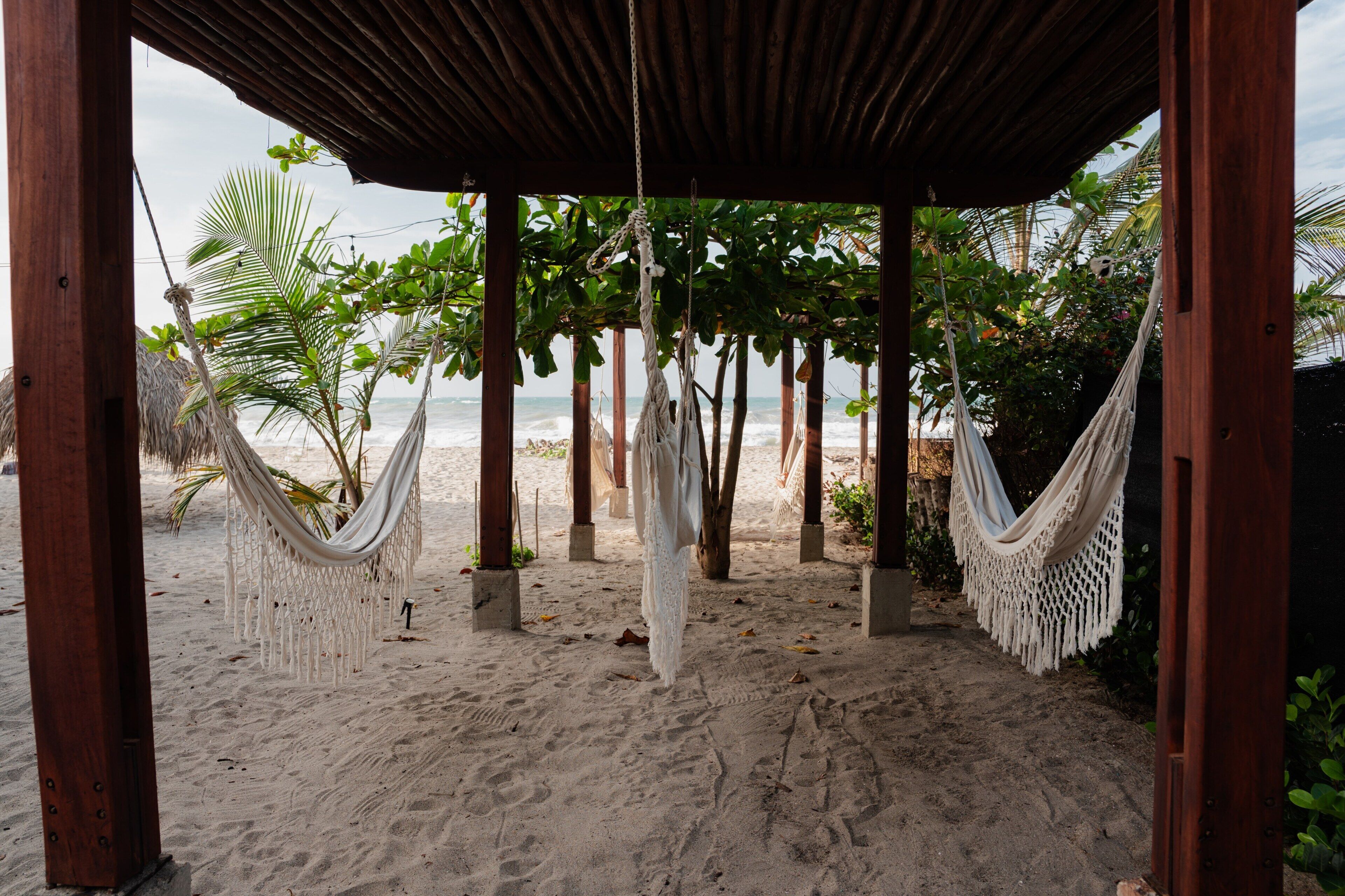 A beach scene with a wooden structure, hammocks, and palm trees.