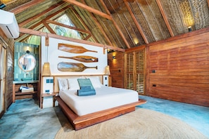 A bedroom with a wooden ceiling, a bed with a white mattress, a nightstand, a mirror, and a wall with wooden paddles. - Casa Iwana Tayrona (Santa Marta)