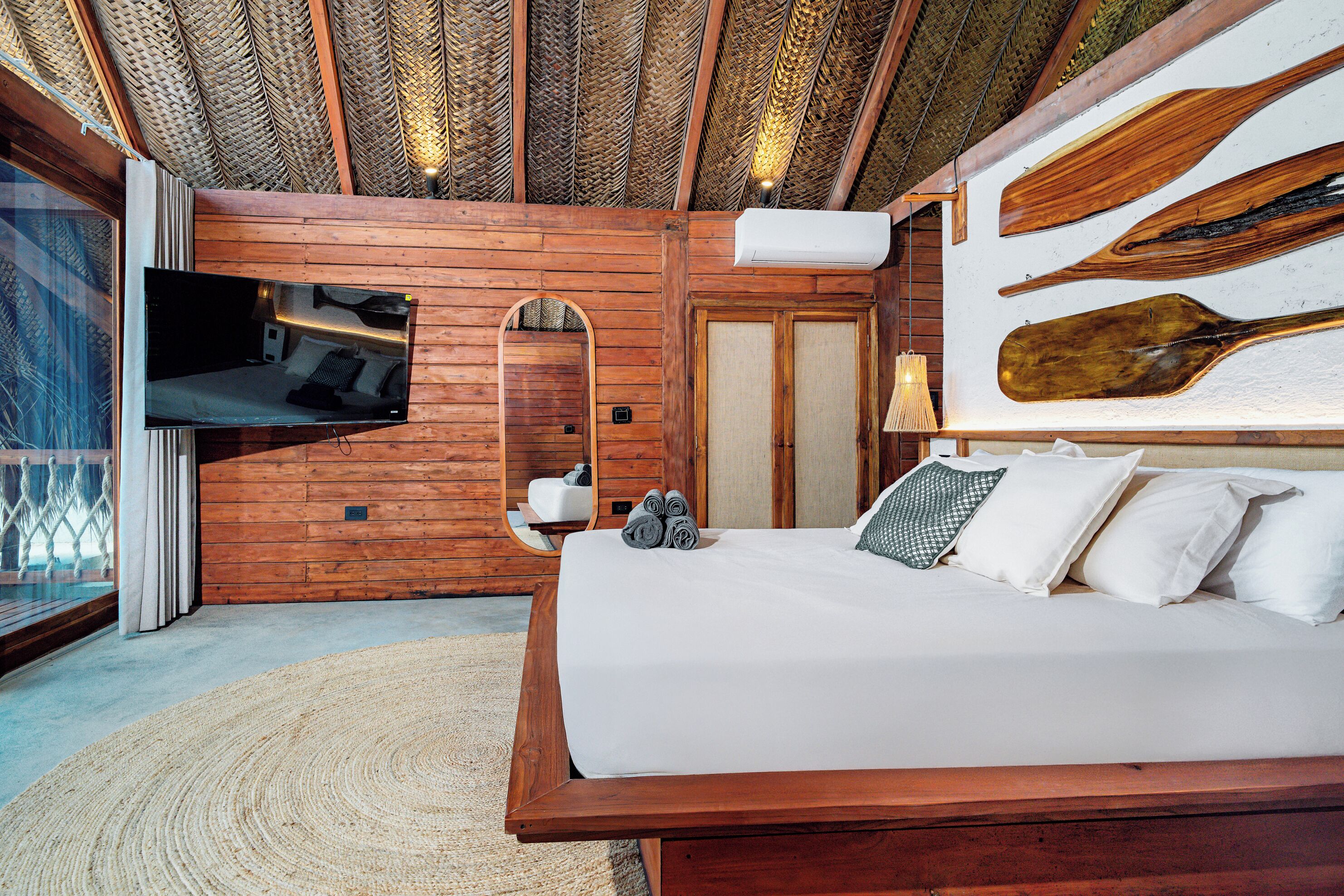 A wooden room with a bed, a mounted TV, and a large mirror.