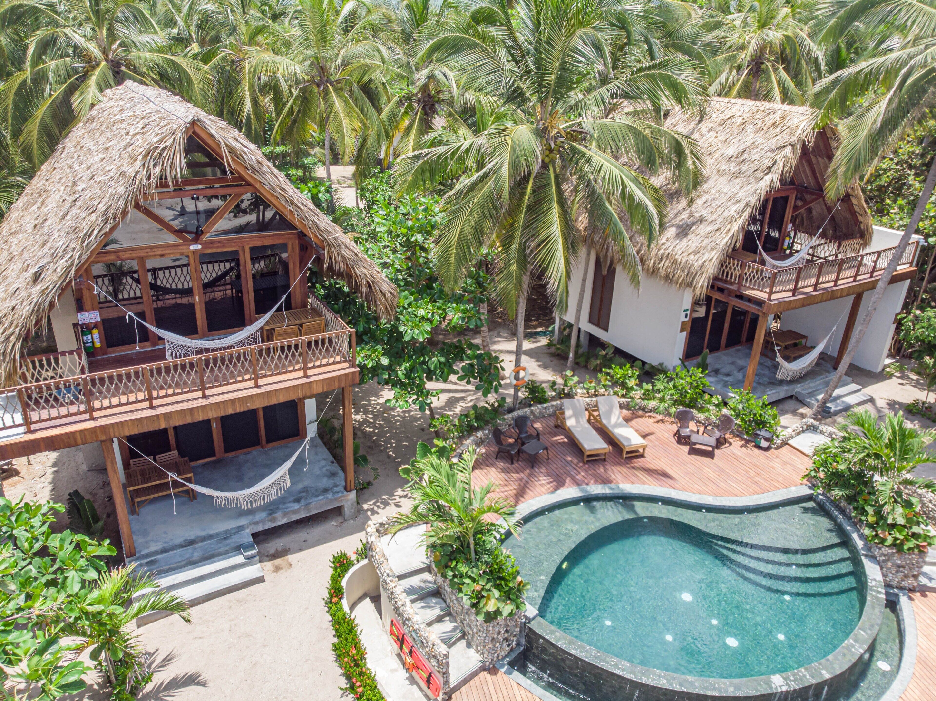 A resort with thatched-roof bungalows, a swimming pool, and lush tropical vegetation.