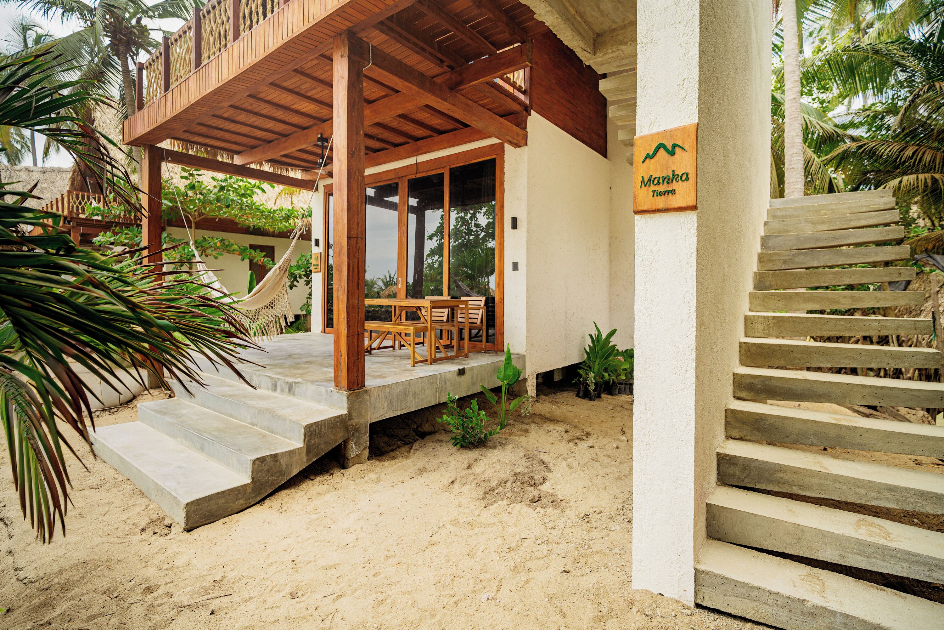 A wooden deck with a table and chairs, a sign reading "Manka Tierra", and a staircase leading up to the deck.