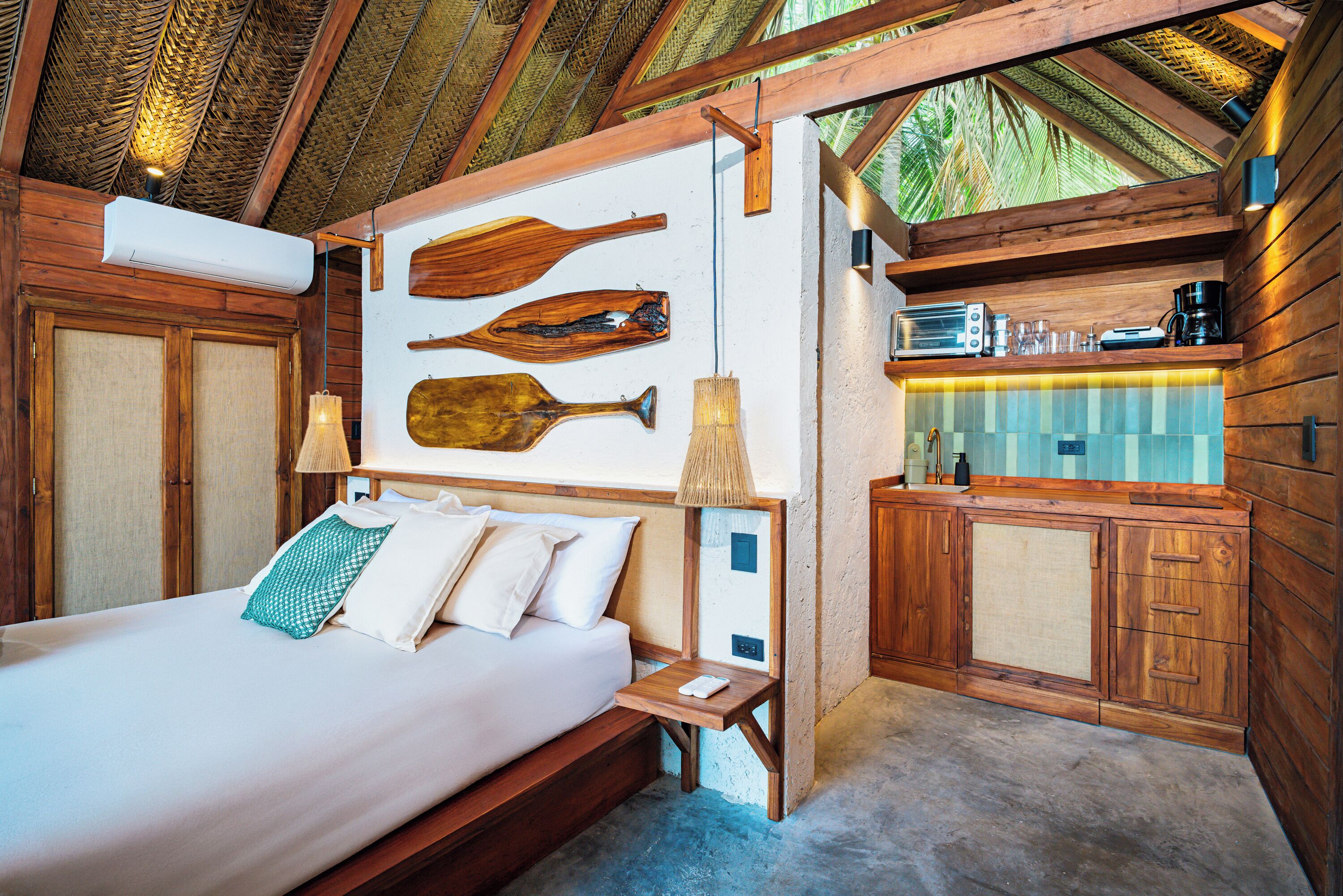 Una habitación con piso de madera, una cama, una mesita y una kitchenette.