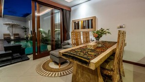 Un salon moderne avec une piscine, un coin repas doté d’une table en bois et une porte-fenêtre coulissante donnant sur un balcon.