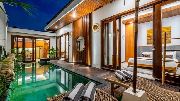 Un espace piscine extérieur moderne, doté d’une chaise longue et de serviettes, d’une terrasse en bois et d’une chambre avec un lit et vue sur la piscine.