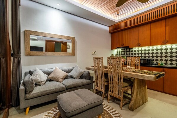 A modern living room with a grey sofa, wooden dining table, and chairs.
