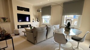Een moderne woonkamer met een bank, twee fauteuils, een glazen salontafel en een flatscreen televisie die aan de muur is bevestigd.