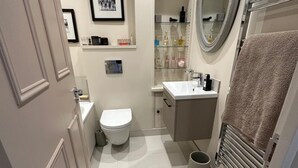 Een kleine badkamer met toilet, wastafel en planken met toiletartikelen.