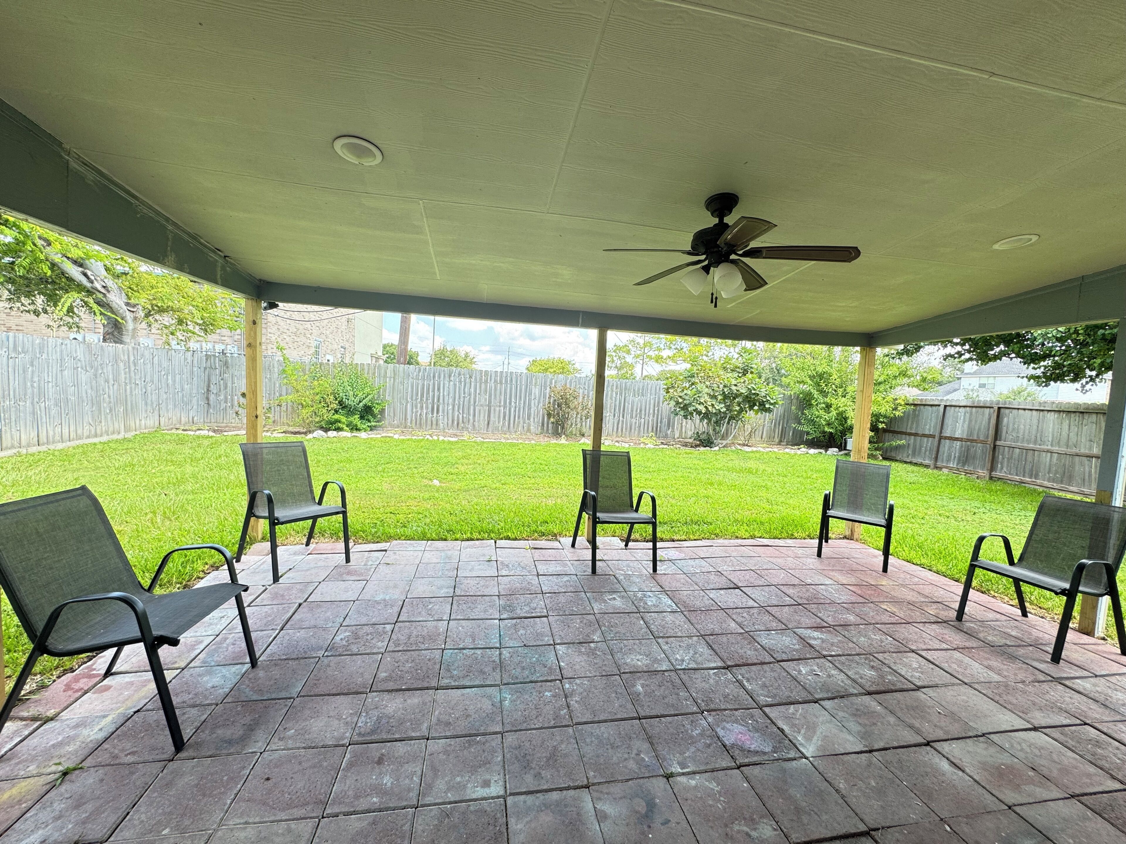 A covered patio area with four chairs and a ceiling fan.
