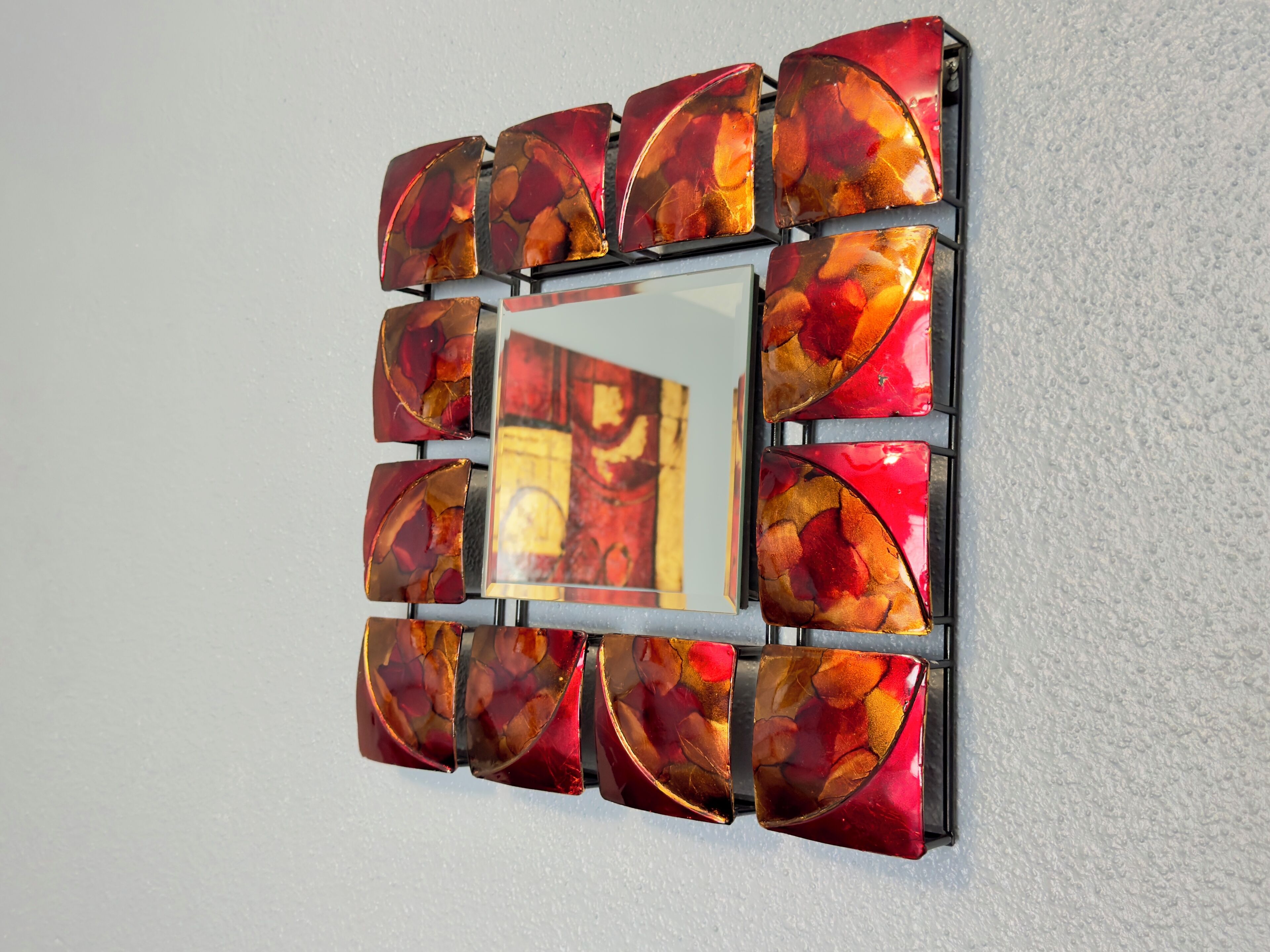 Un miroir mural doté d’un cadre aux motifs géométriques.