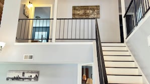 A multi-level interior with a staircase, a cityscape artwork, and a light fixture. - Spacious Home Sleeps 12 - World Cup Ready (Houston)