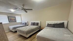 Een kamer met drie bedden, een plafondventilator en een schilderij aan de muur.