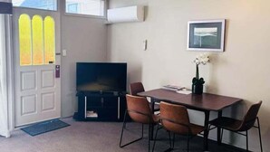 Une pièce comprenant une table à manger, quatre chaises, un téléviseur à écran plat, une petite plante en pot et un tableau encadré accroché au mur.