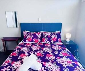 Ein Bett mit einer blumigen Tagesdecke, einem weißen Kopfkissen und einem blauen Kopfteil.