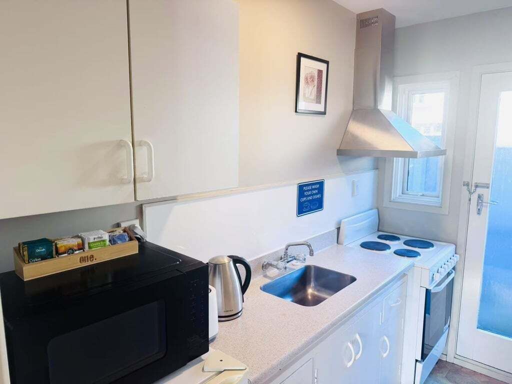 A compact kitchen with a microwave, kettle, sink, and stove.