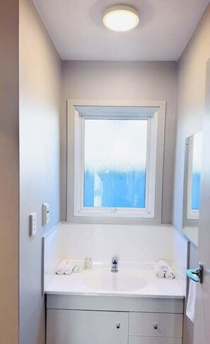 Ein Badezimmer mit weißem Waschtisch, einem Fenster und einem Spiegel.