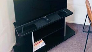 Une pièce avec un téléviseur à écran plat posé sur un meuble noir, un climatiseur blanc fixé au mur et une chaise sur la droite.