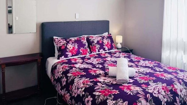 Une chambre d’hôtel avec un lit, une table de chevet, un miroir et une fenêtre avec des rideaux.