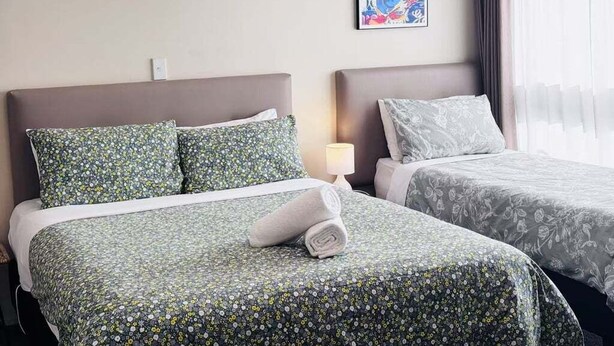 A hotel room with two beds, each with floral-patterned bedding, a wall-mounted light, and a colorful abstract painting.