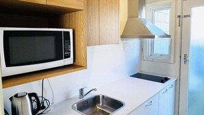 A compact kitchen with a microwave, stainless steel sink, and wooden cabinets.