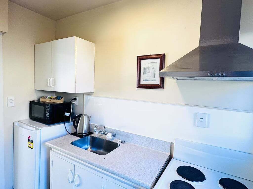 A compact kitchen with a microwave, kettle, sink, and stove.
