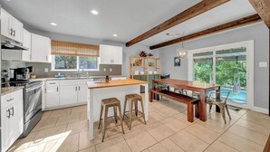 A modern kitchen with white cabinets, a wooden island, and a dining area with a bench and chairs.