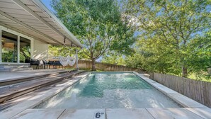 A rectangular swimming pool with a wooden deck and a hammock.
