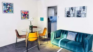 Una habitación moderna con una mesa redonda de vidrio, dos sillas, un sofá color turquesa y una obra de arte en la pared.