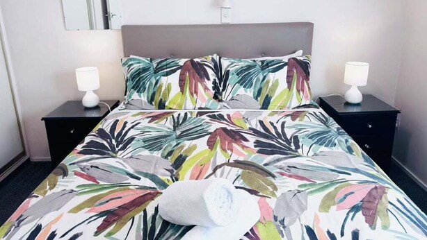 Una cama bien hecha con una colcha floral, dos mesitas de noche con lámparas y un espejo en la pared.