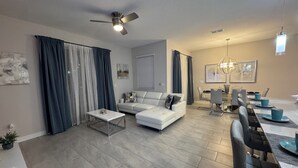 Una sala de estar moderna con un sofá blanco, una mesa de centro y una zona de comedor con una mesa larga y sillas.