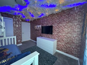 A room with a brick wall, a white dresser, a bed with a blue pillow, and a television mounted on the wall. - 4BR/3BA Townhouse w/ Private Pool in Storey Lake (Kissimmee)